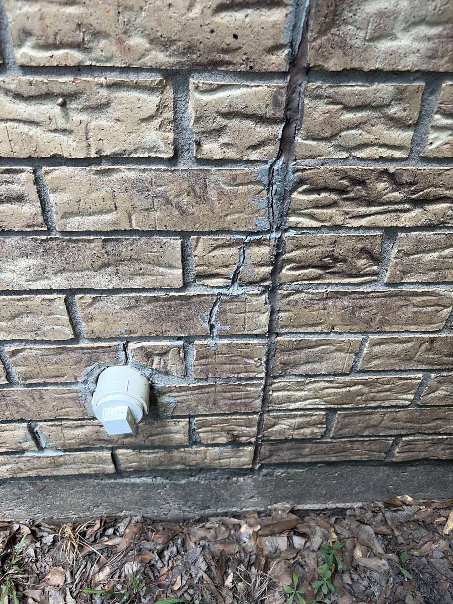 Stair-step crack through brick veneer and mortar joints near the foundation